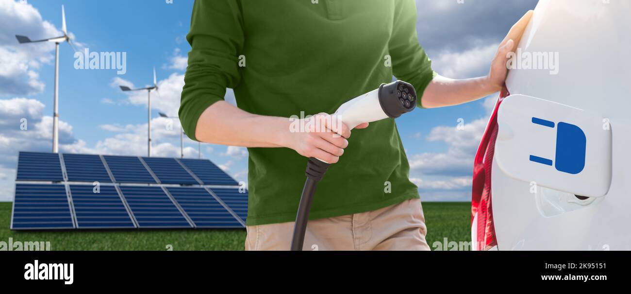 Close up of man with electric car charging cable on the background of solar panels and wind turbines  Stock Photo
