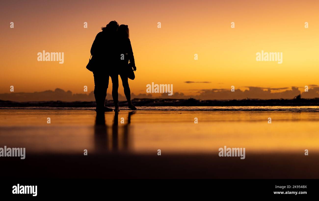 A silhouette of a young couple on the beach during the golden sunset ...