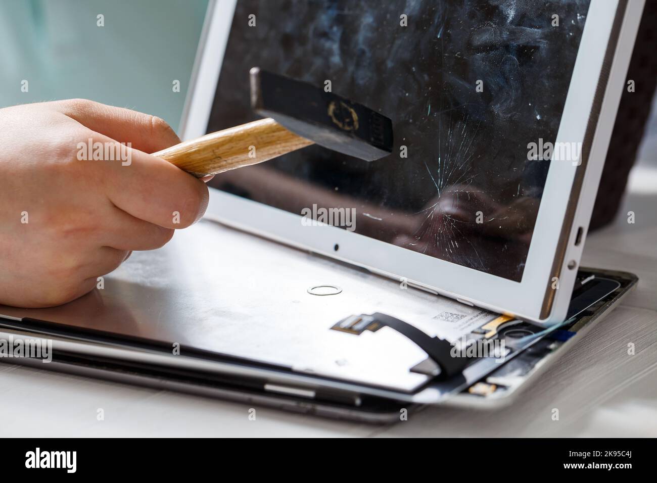 The hammer hits the broken touchscreen tablet, suggesting that it is about to replace it. Broken glass tablet repair Stock Photo
