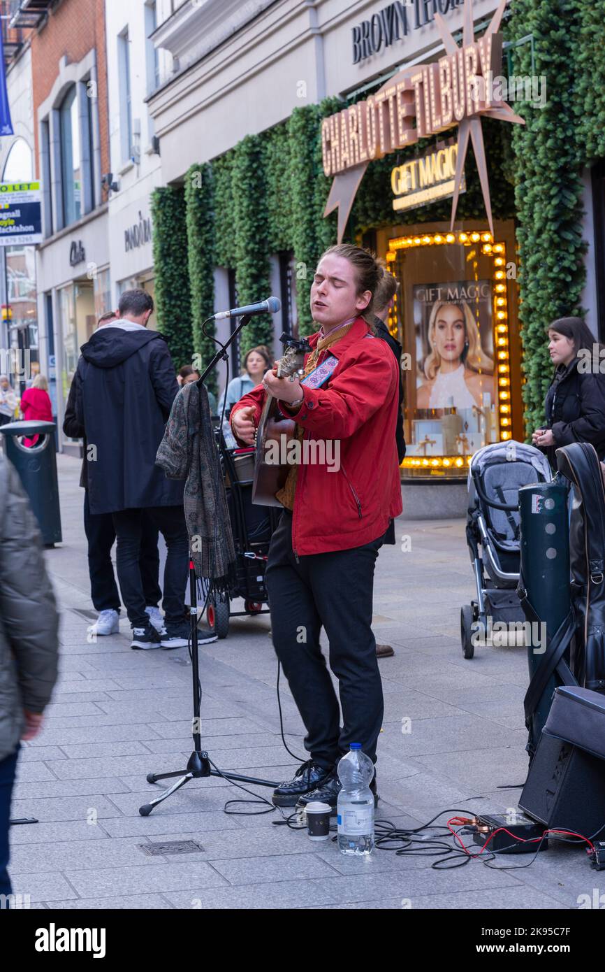 Ireland Eire Dublin Grafton Street busker solo young musician guitar singing playing outside Brown Thomas tourists shoppers microphone water bottle Stock Photo