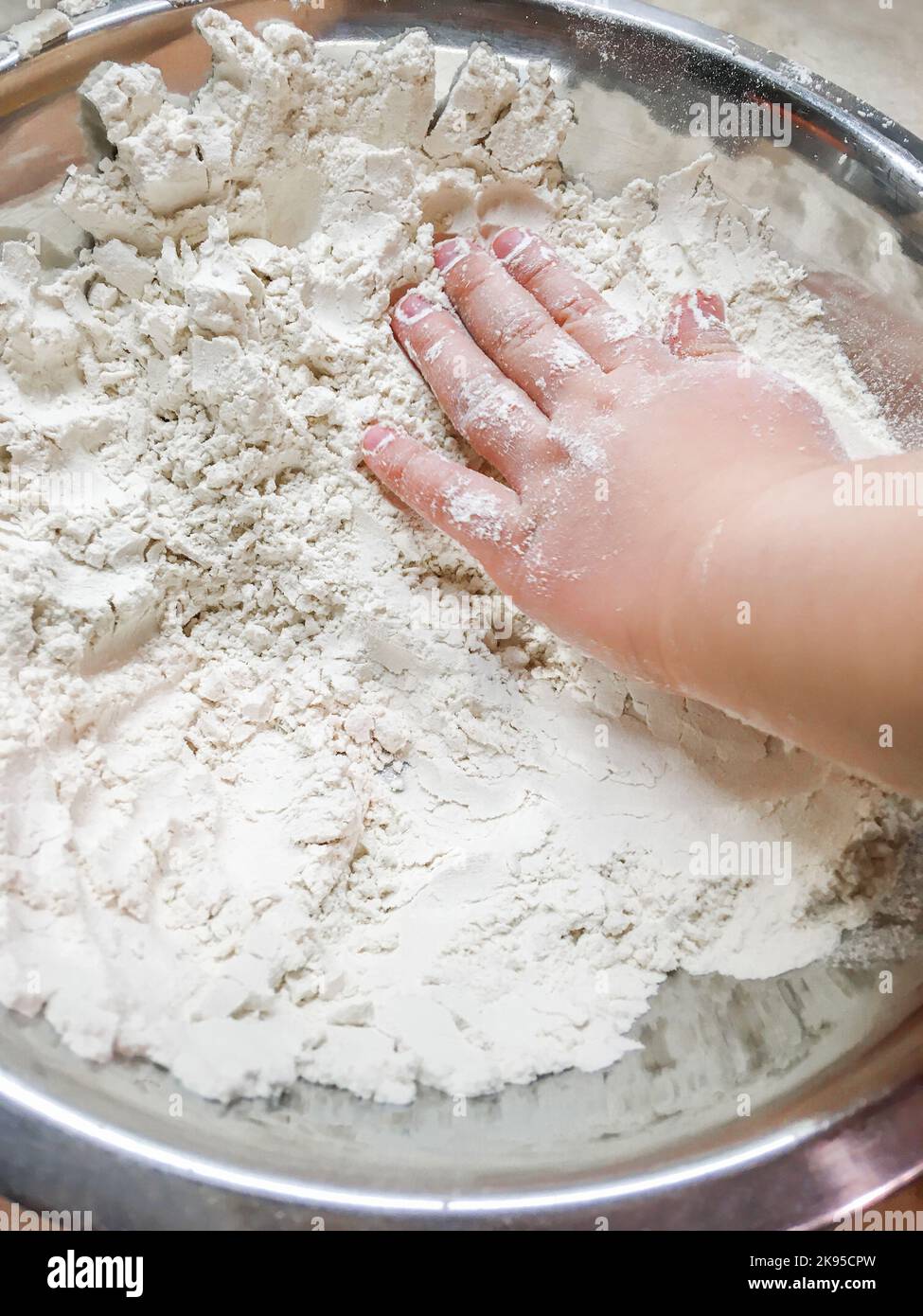 Little child is touching flour in metal bowl. Cooking with children