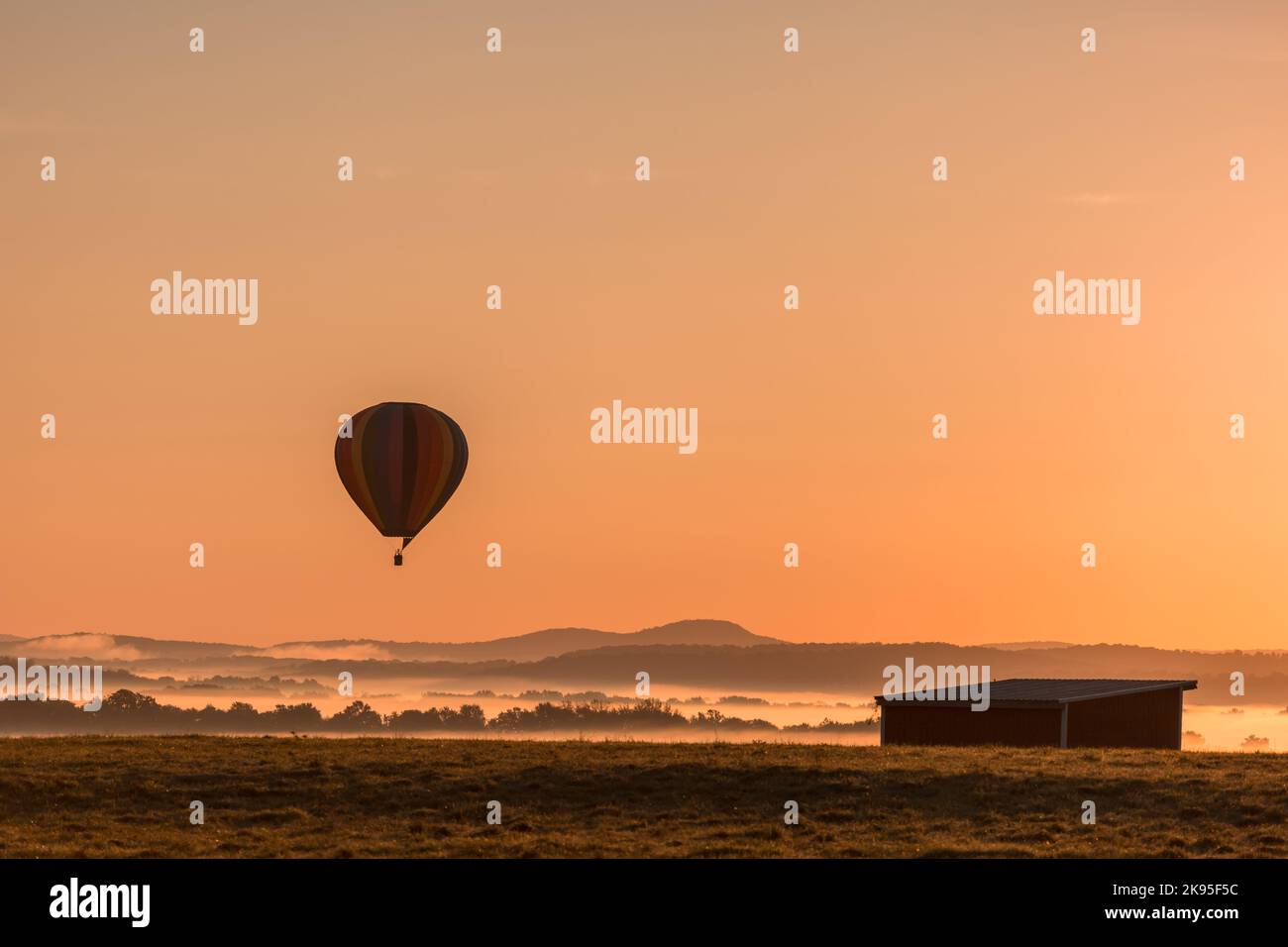 Hot air balloon is basked in a golden glow as it slowly ascends over a ...