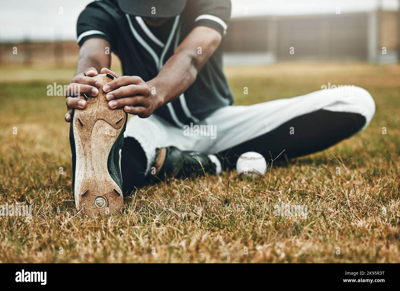 Baseball, player and stretching for game, training and workout on field, with ball and sportswear for health. Black man, athlete or doing exercise to Stock Photo