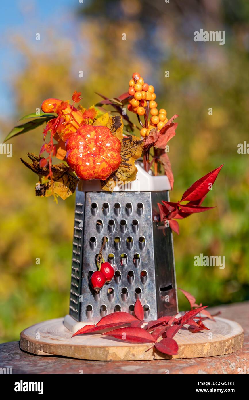 A four-sided grater has been decorated with autumn flowers, plants and leaves, on a bokeh background Stock Photo