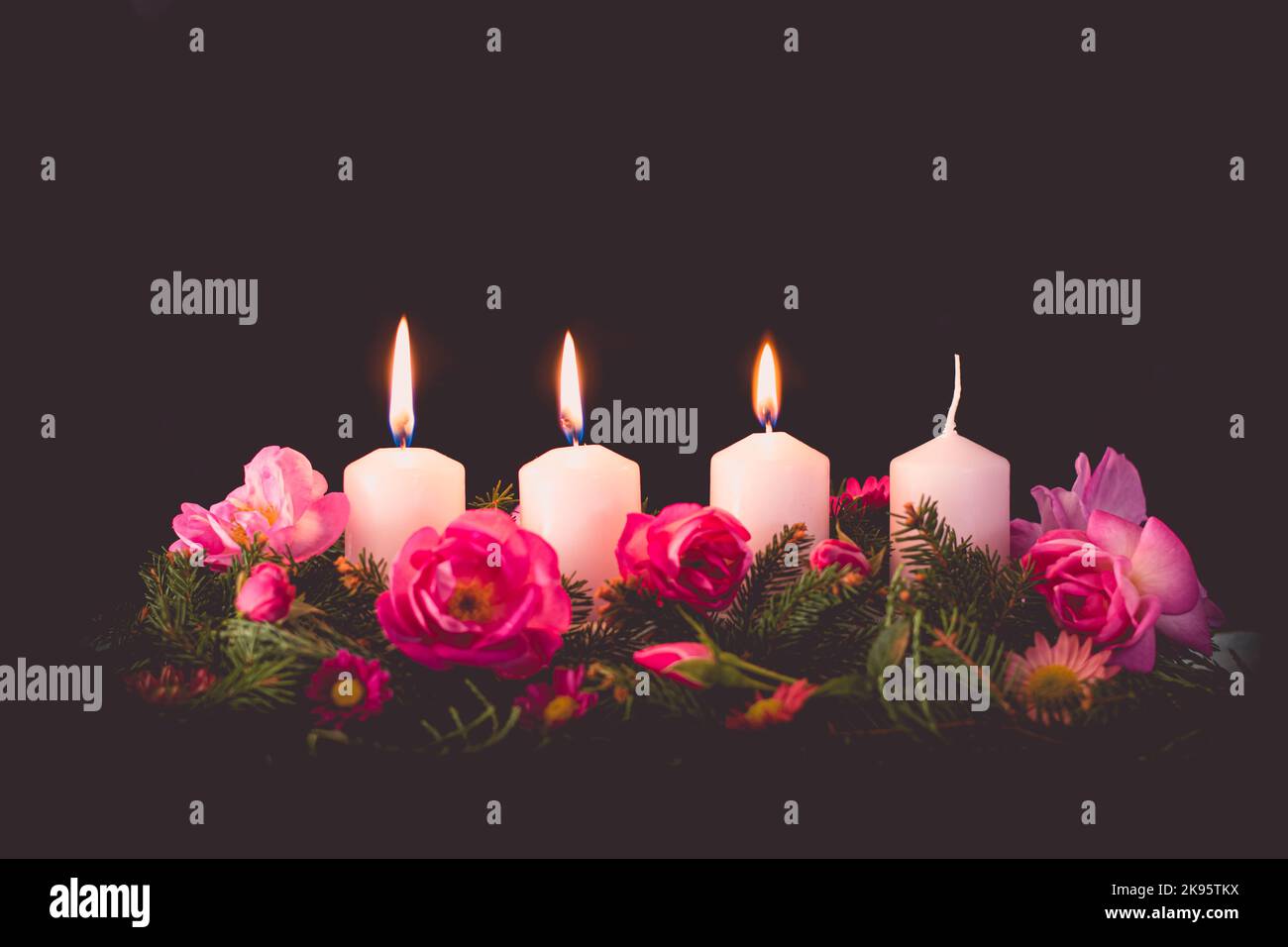 third burning advent candle on decorated rose flower pink advent wreath