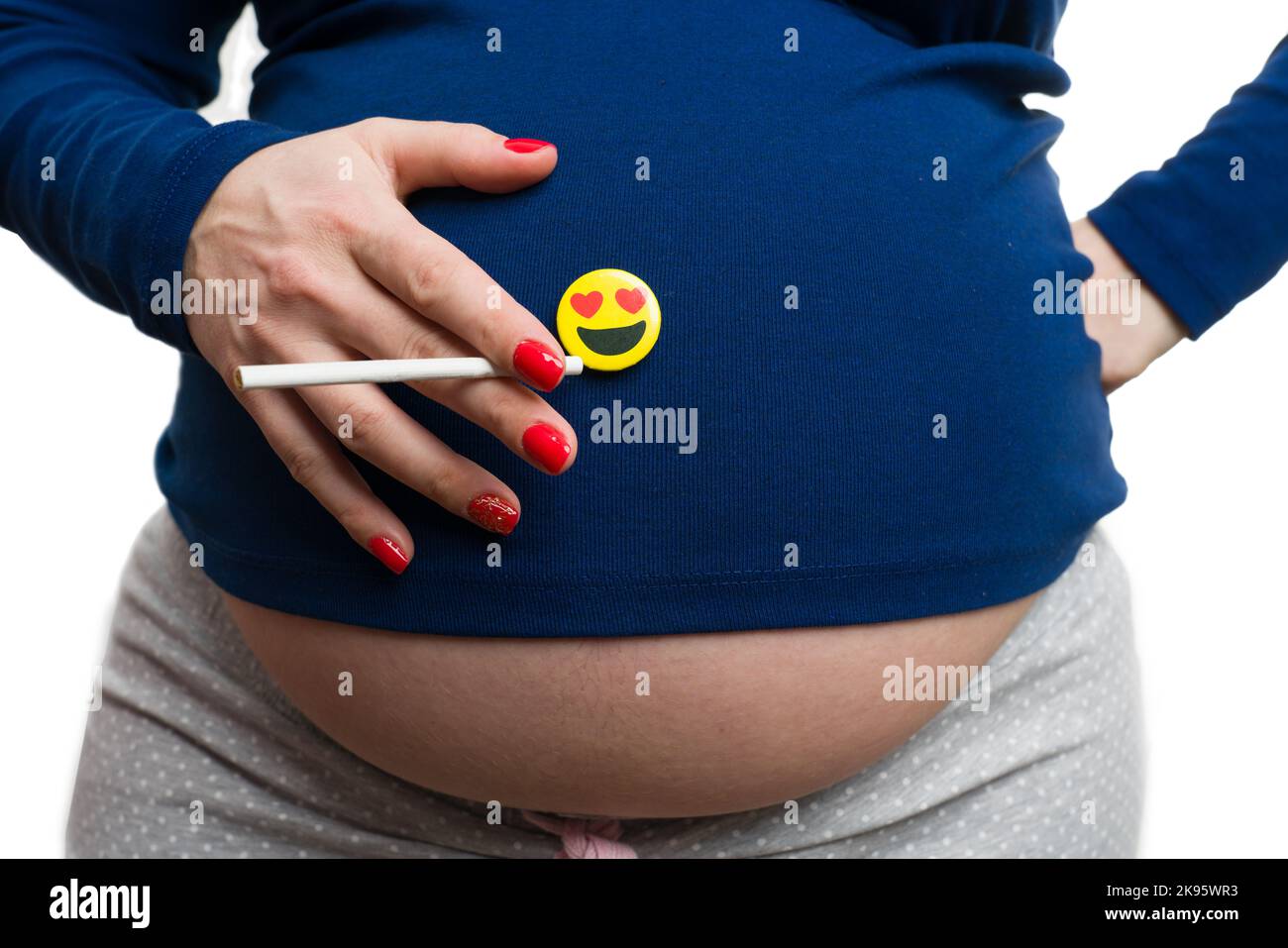 Close-up of pregnant woman holding cigarette and heart eyes emoji on belly  isolated on white studio background Stock Photo