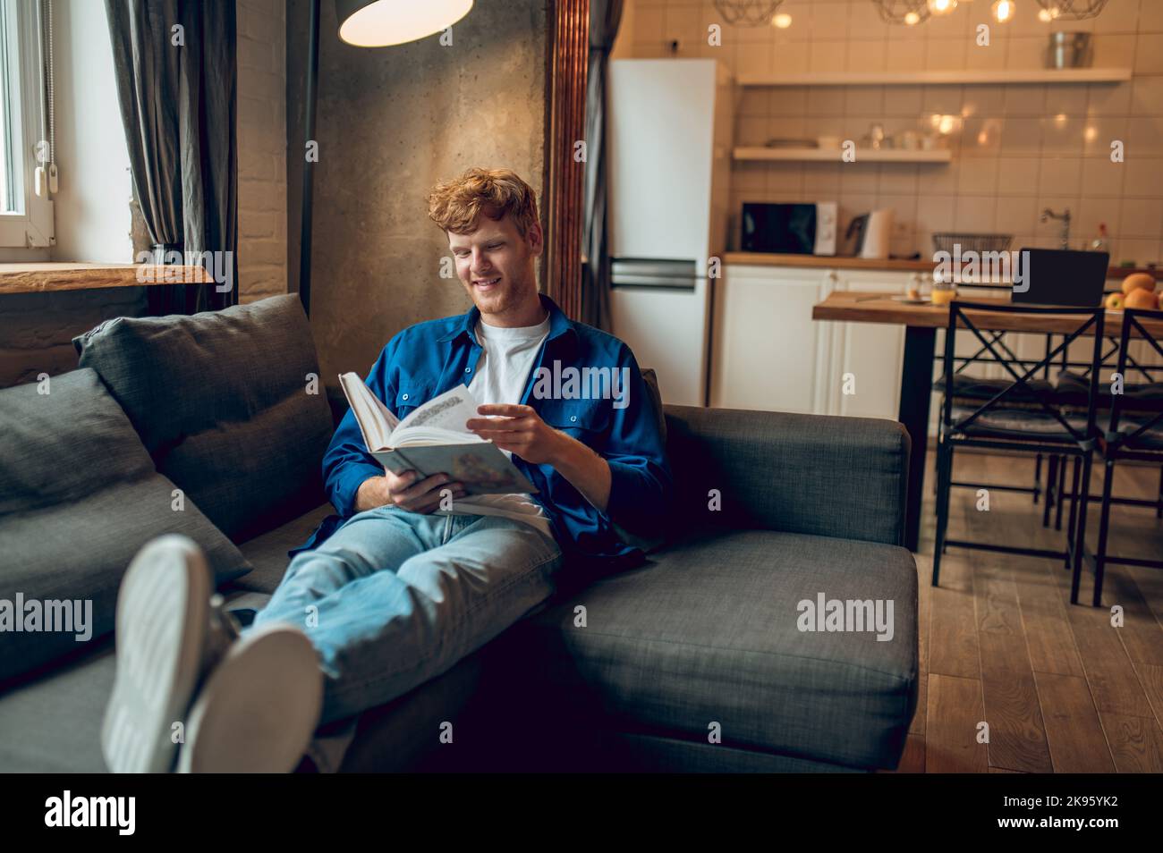 Ginger young man sitting at home at the window with a book Stock Photo