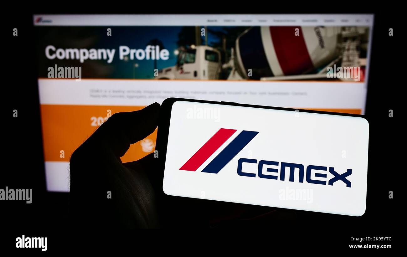 Person holding smartphone with logo of Mexican materials company CEMEX S.A.B. de C.V. on screen in front of website. Focus on phone display. Stock Photo