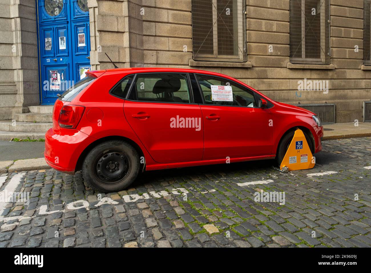 Republic of Ireland Eire Dublin City Council street scene red car clamped yellow wheel clamp in loading bay with warning sticker in English & Gaelic Stock Photo