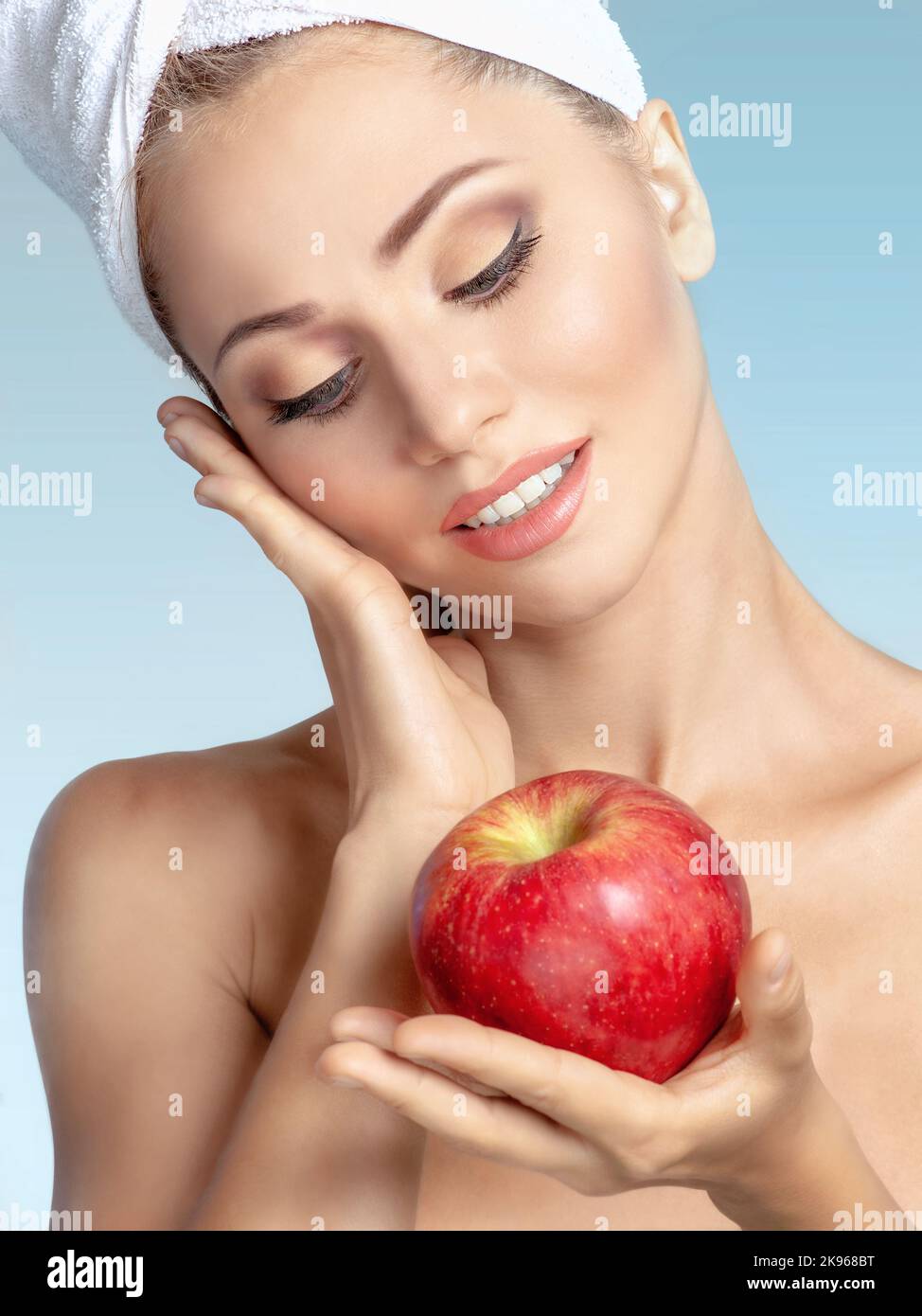 Close-up face of young beautiful smiling woman in towel on head holding red apple. Natural beauty, spa, skin care, cosmetics concept Stock Photo