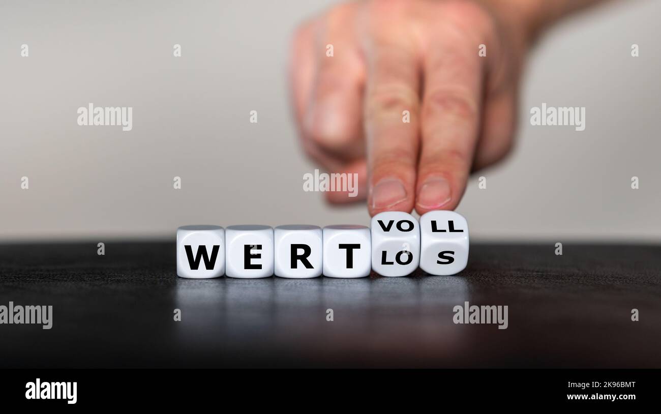 Hand turns dice and changes the German word 'wertlos' (worthless) to 'wertvoll' (valuable). Stock Photo