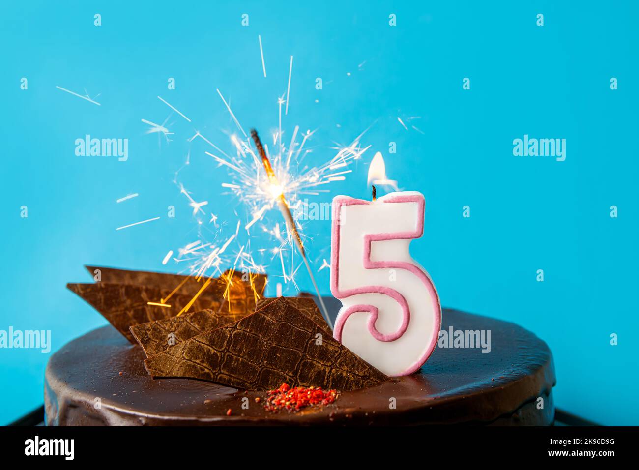 Number 5 birthday candle burning and sparkler with sparks fly on cake. The fifth birthday or anniversary celebration concept. Lot of copy space. Stock Photo
