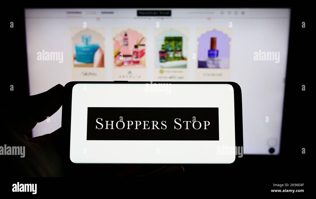 Person holding smartphone with logo of Indian retail company Shoppers Stop Limited on screen in front of website. Focus on phone display. Stock Photo