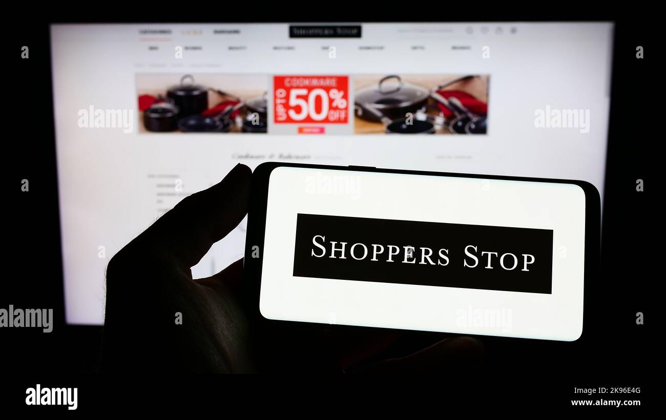 Person holding cellphone with logo of Indian retail company Shoppers Stop Limited on screen in front of business webpage. Focus on phone display. Stock Photo
