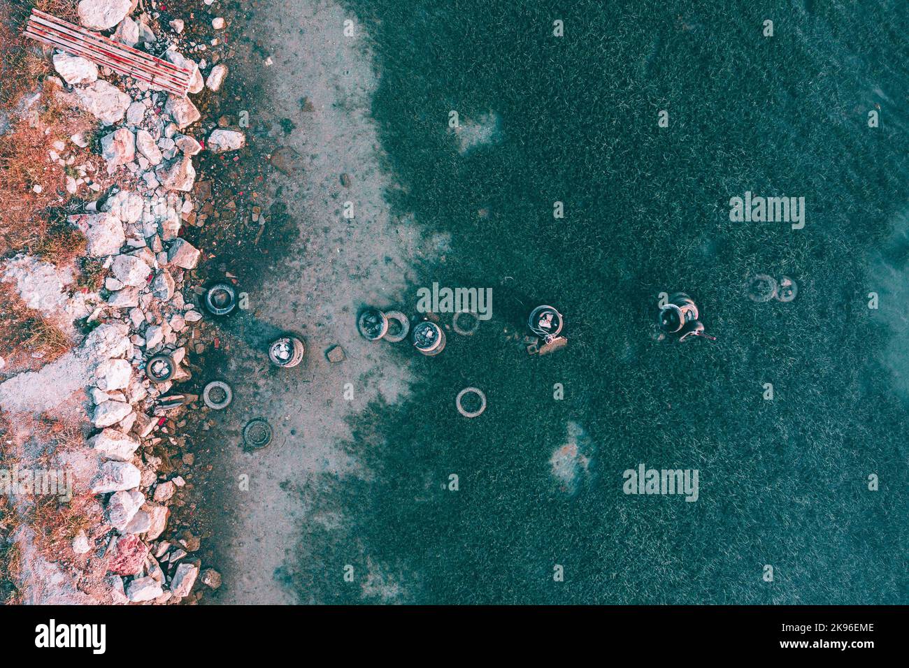 An aerial top view of dirty trash tires and rocks on the shore of Evoia, Greece Stock Photo