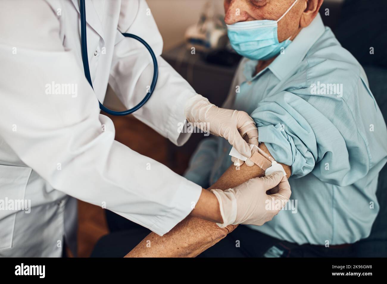 Doctor putting a plaster in place of injection of vaccine to senior man ...