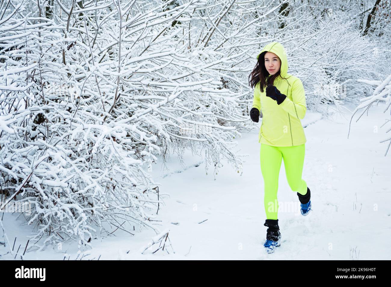 Cold Weather Running. Happy woman running in winter snowy park, forest. Running athlete woman sprinting during winter training outside in cold snow Stock Photo