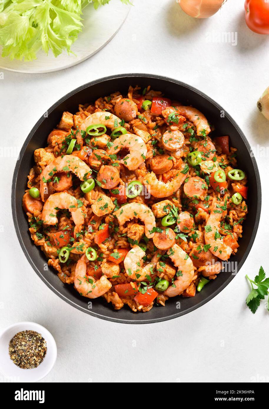 Creole jambalaya with smoked sausages, chicken meat and vegetables in pan over white stone