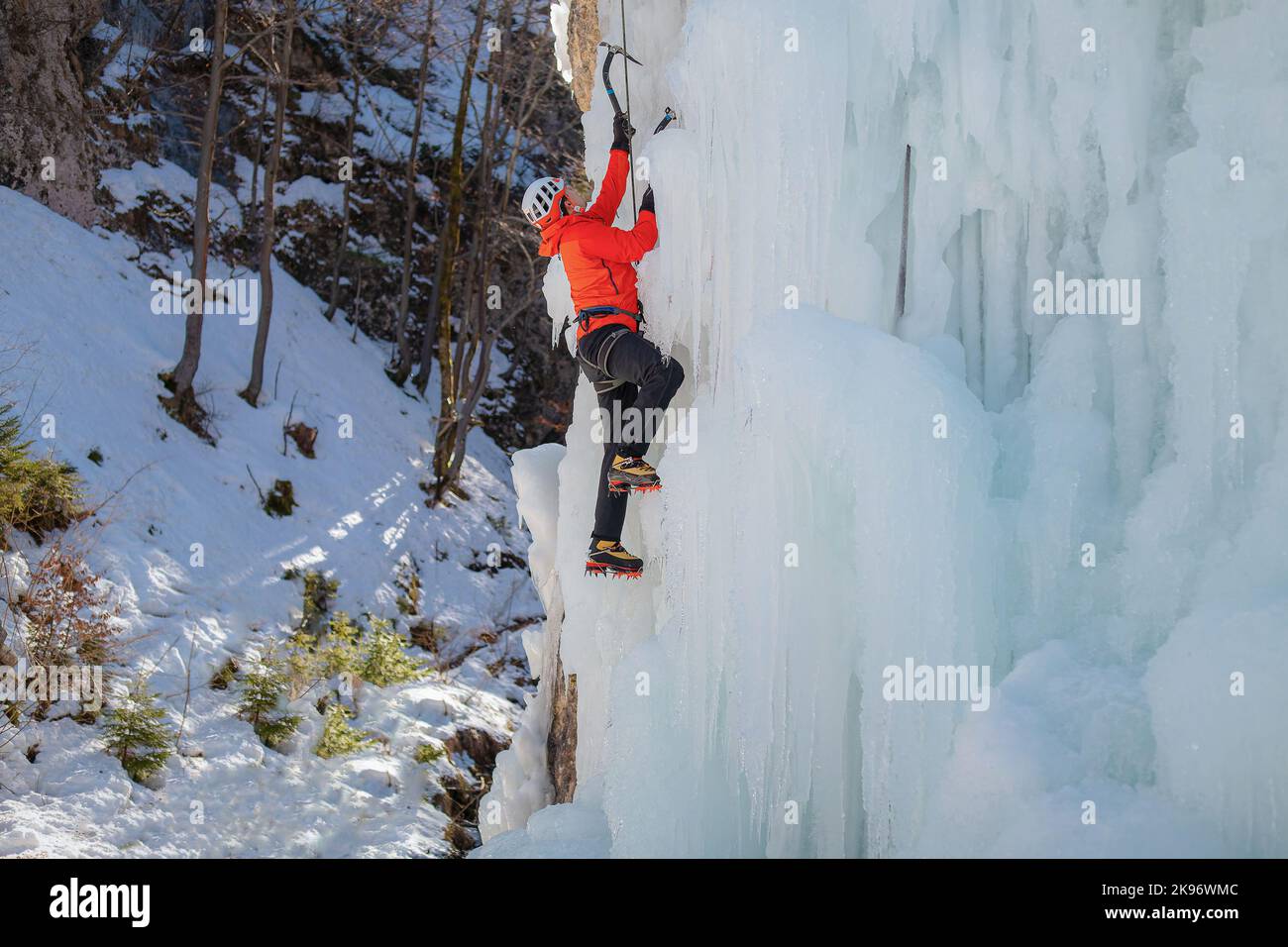 Alpinist man with ice climbing equipment on a frozen waterfall Stock