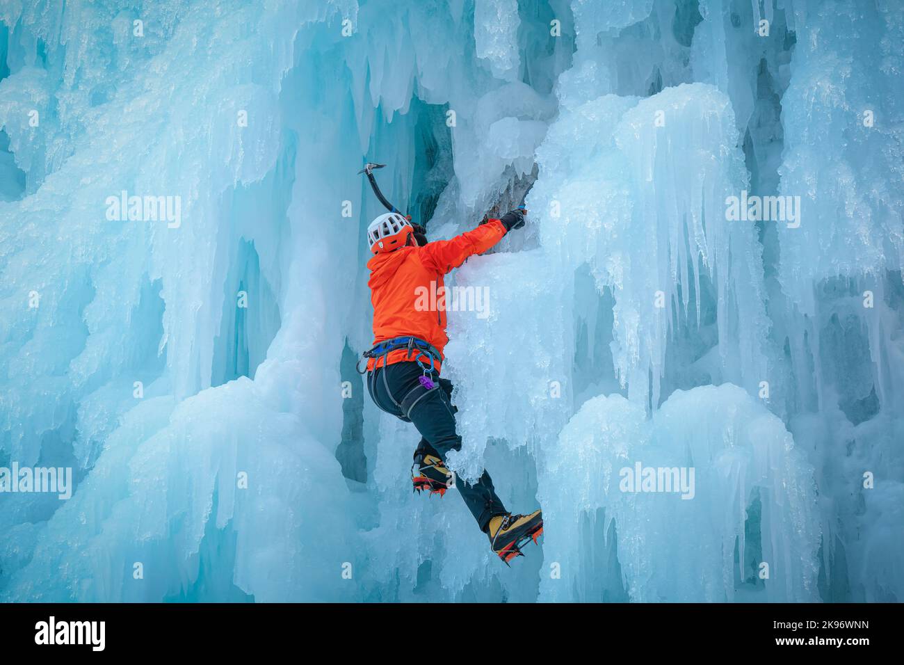 Alpinist man with ice climbing equipment on a frozen waterfall Stock