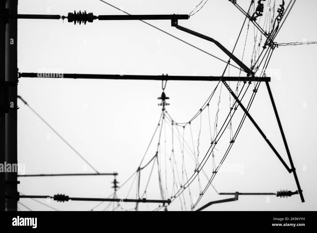 Overhead lines of a railway are under white sky, monochrome silhouette photo Stock Photo