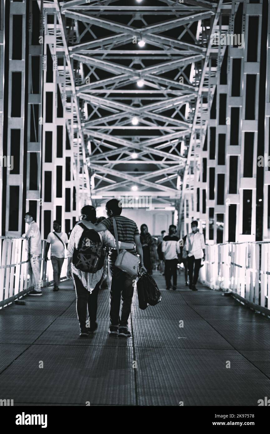 A vertical grayscale shot of people walking on a bridge in Babughat, Kolkata in the evening Stock Photo