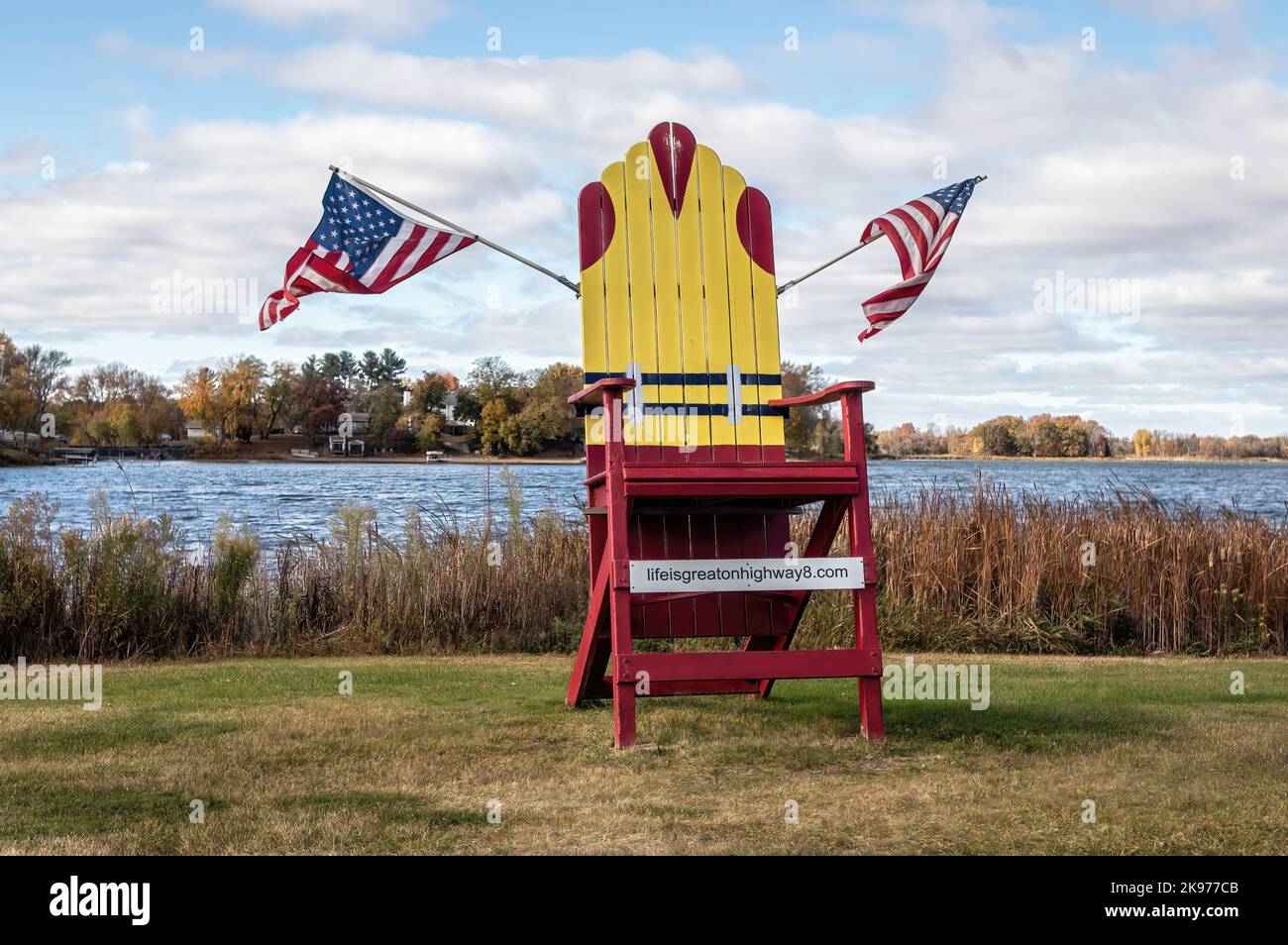 Big red chair on North Center Lake with a PFD on it due to being blown into the lake, with two American flags in Center City, Minnesota USA. Stock Photo