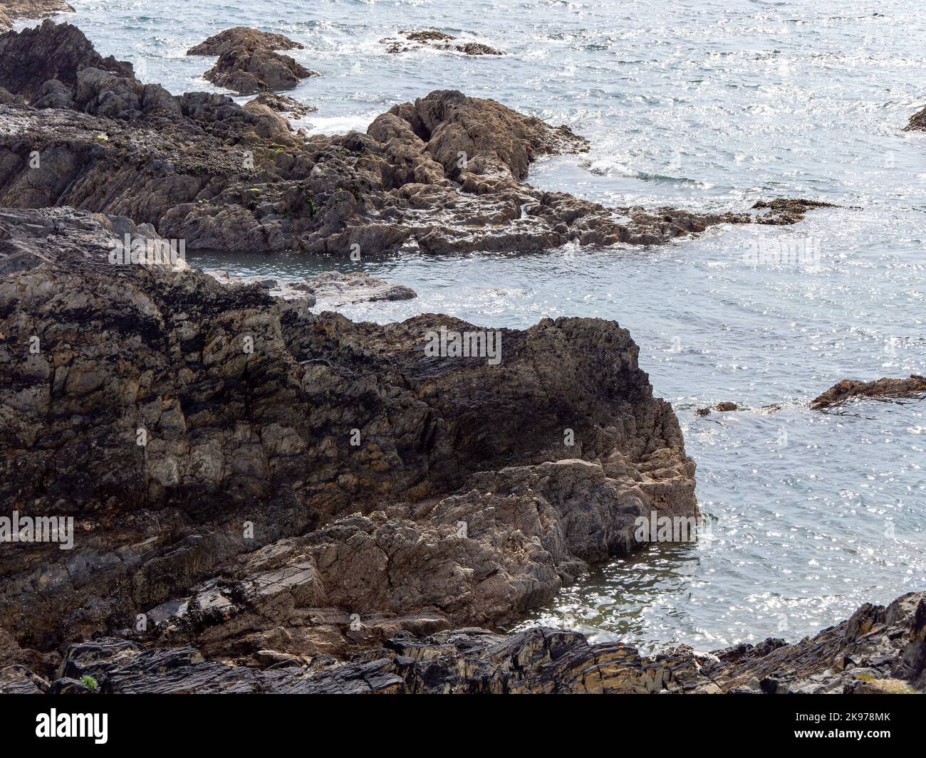 Exposed rocks on the shore. Seaside in sunny weather, rock formation near body of water. Stock Photo