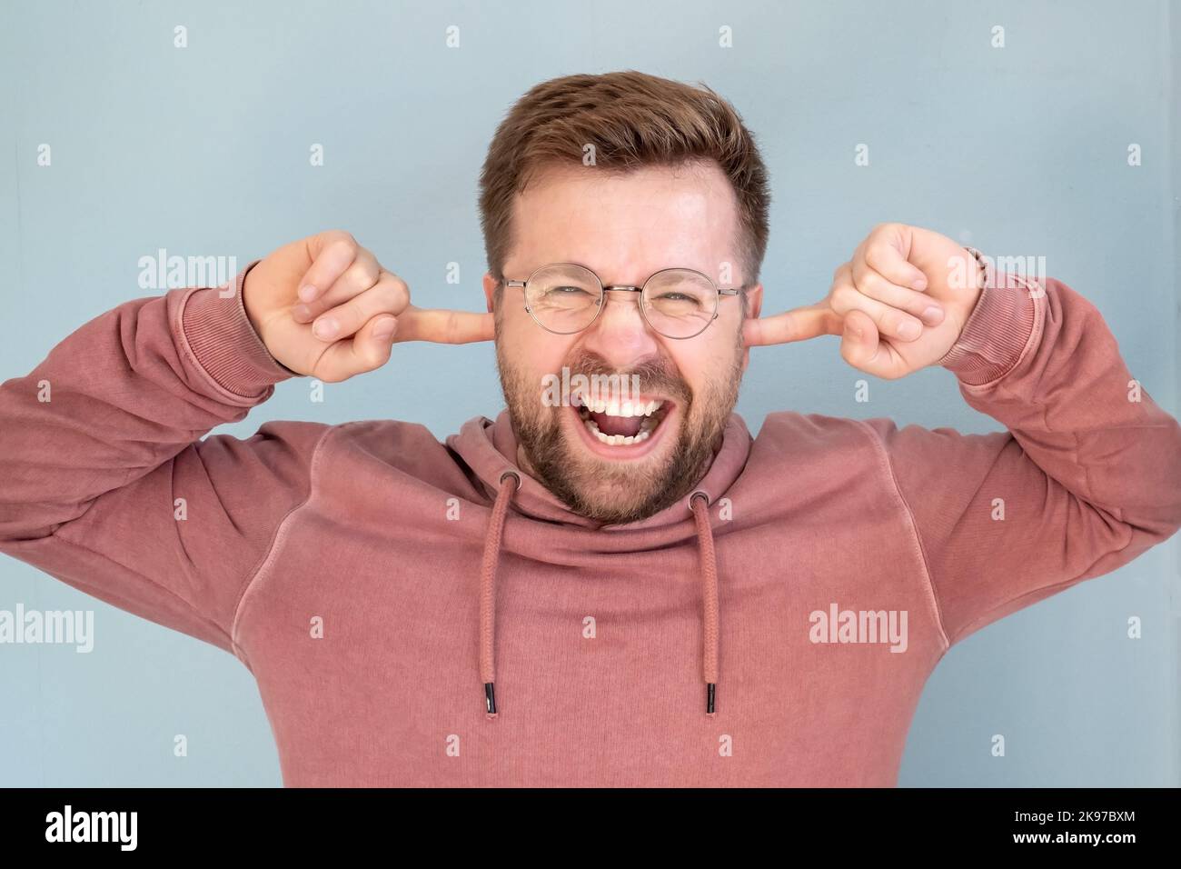 Happy man covered ears with fingers while standing on a blue background. Stock Photo