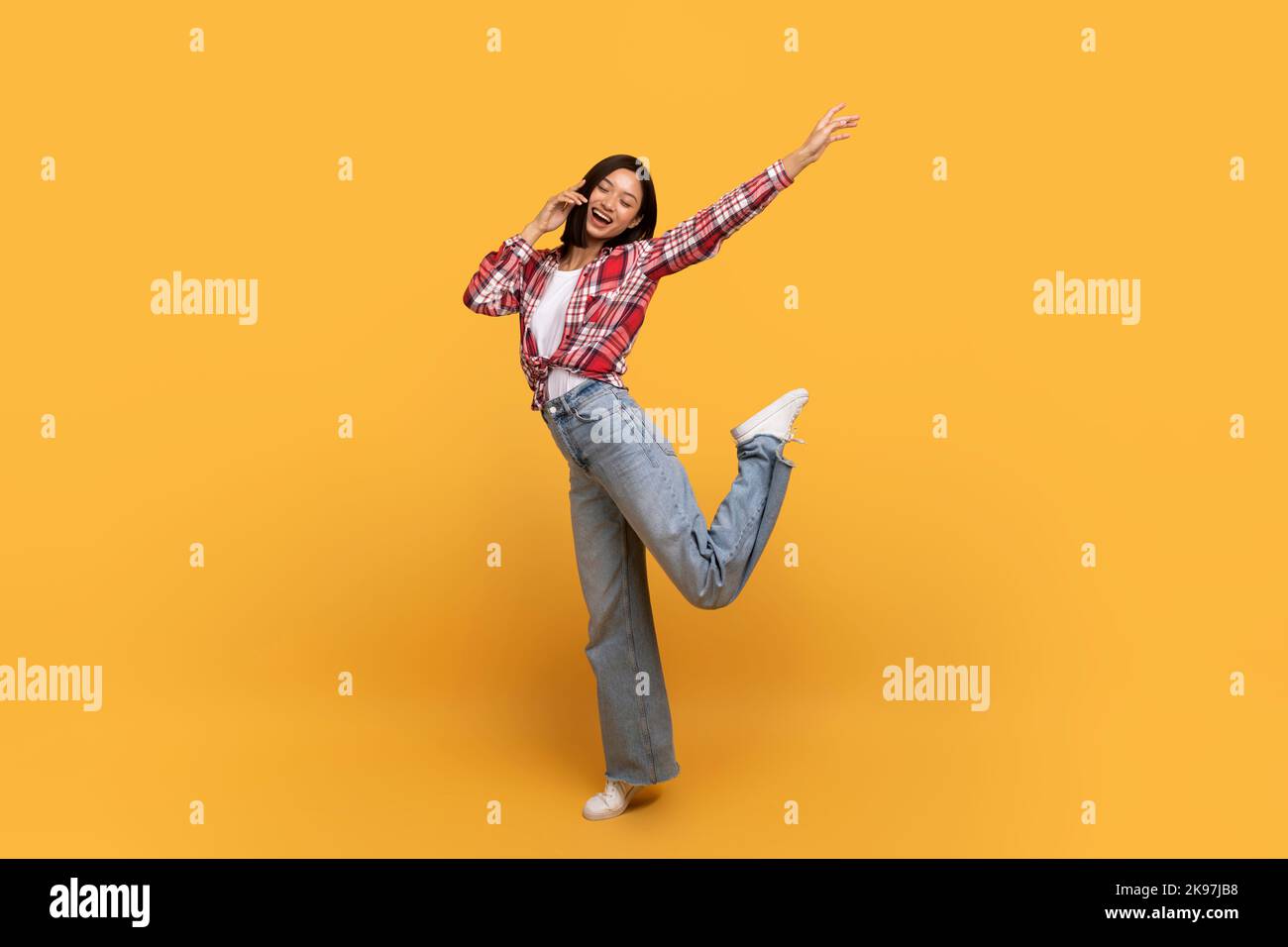 Full body length shot of happy asian lady jumping, dancing and fooling around, being in good mood, yellow background Stock Photo