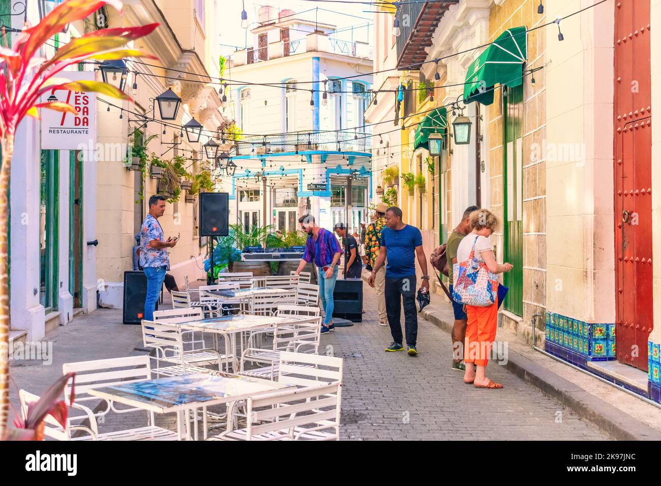 Cuban people setting patio restaurant tables in an Old Havana alley. Incidental tourists are also in the scene. Stock Photo