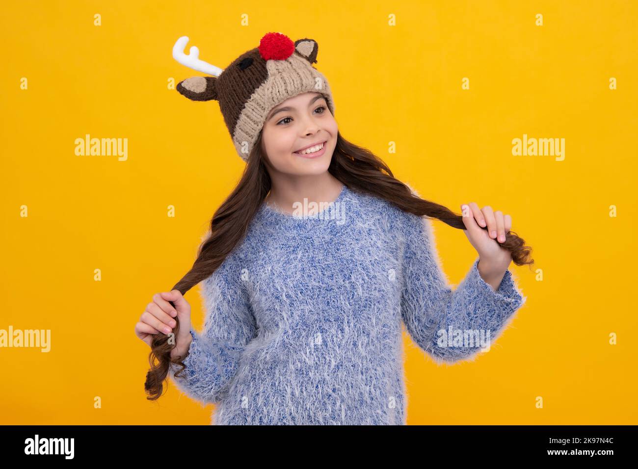 Modern teen girl wearing sweater and knitted hat on isolated yellow background. Happy girl face, positive and smiling emotions. Stock Photo