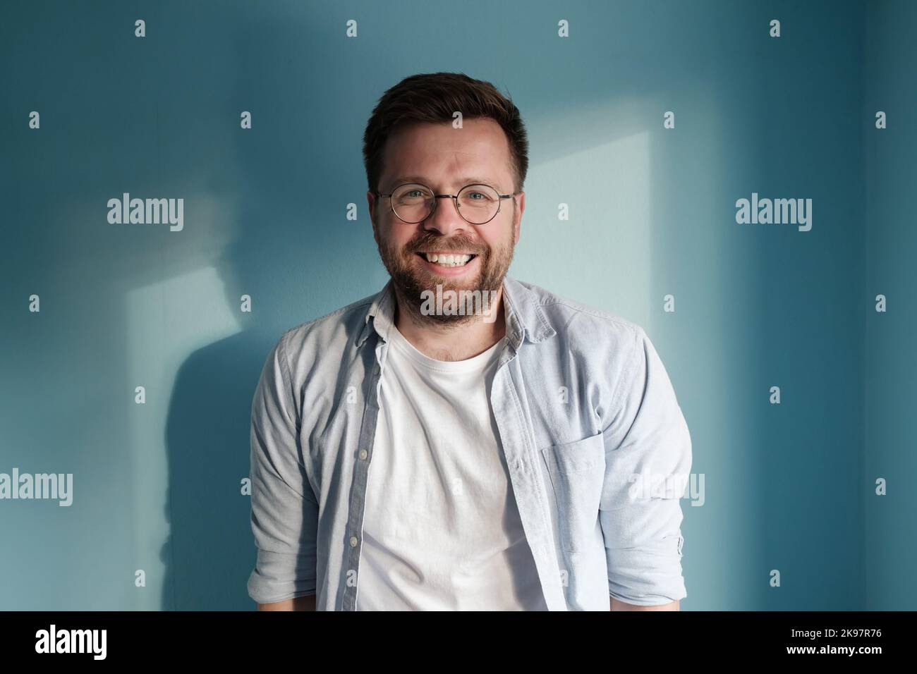 Charming young man smiling leaning against a blue wall Stock Photo - Alamy