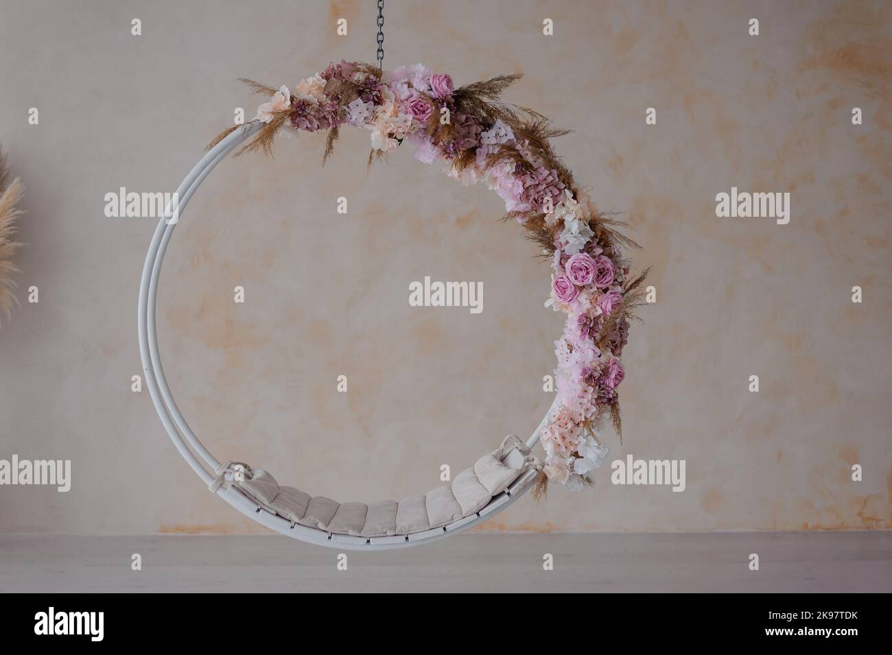 White swing on a chain, decorated with pink flowers. Vase in the background Stock Photo