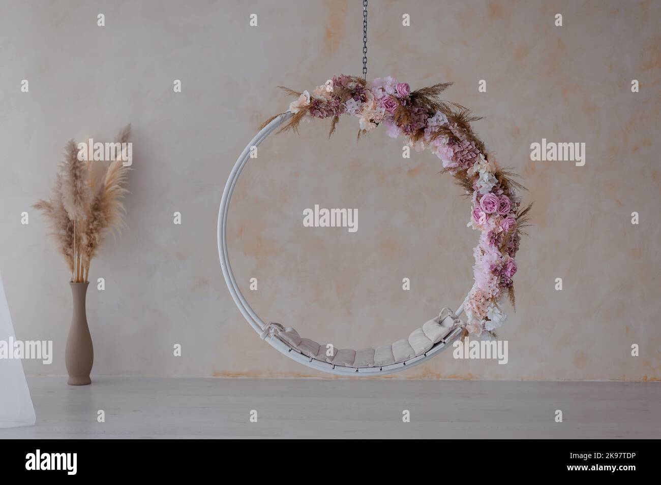 White swing on a chain, decorated with pink flowers. Vase in the background Stock Photo