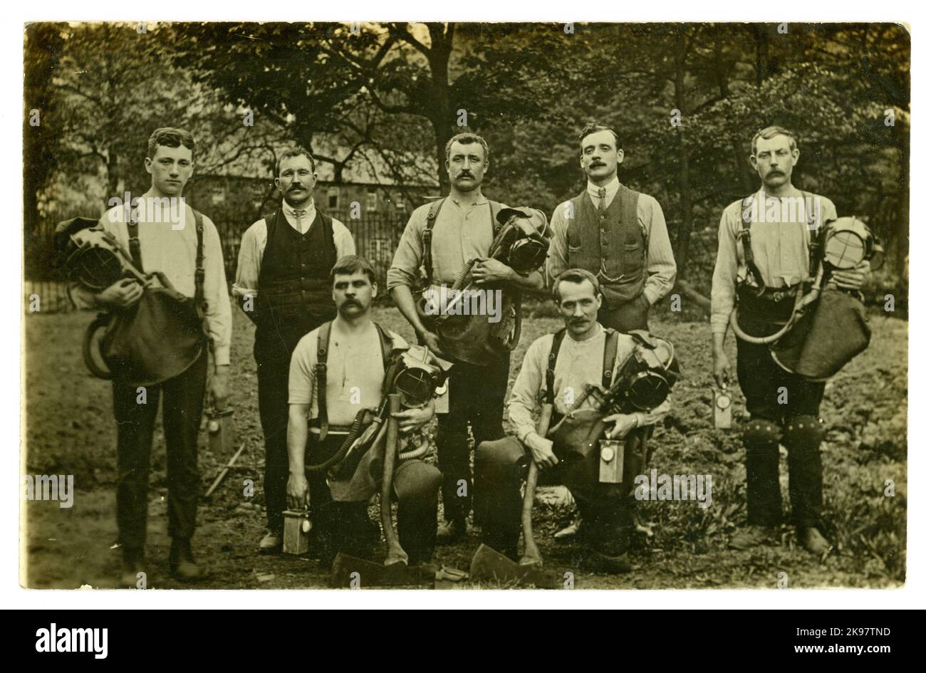 Original early 1900's postcard of coal mining pit rescue team with axes and holding breathing apparatus in form of Draeger /Drager smoke helmets with attached breathing bag covered by a leather flap, together with lamps, protective knee pads and a saw (in foreground) they were well equipped to respond if disaster occurred. Circa 1919, U.K. Stock Photo