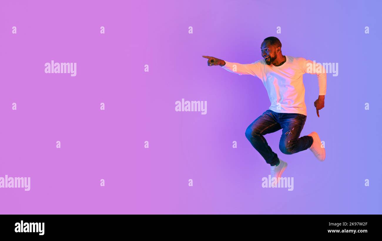 Excited black man jumping and pointing at copy space Stock Photo