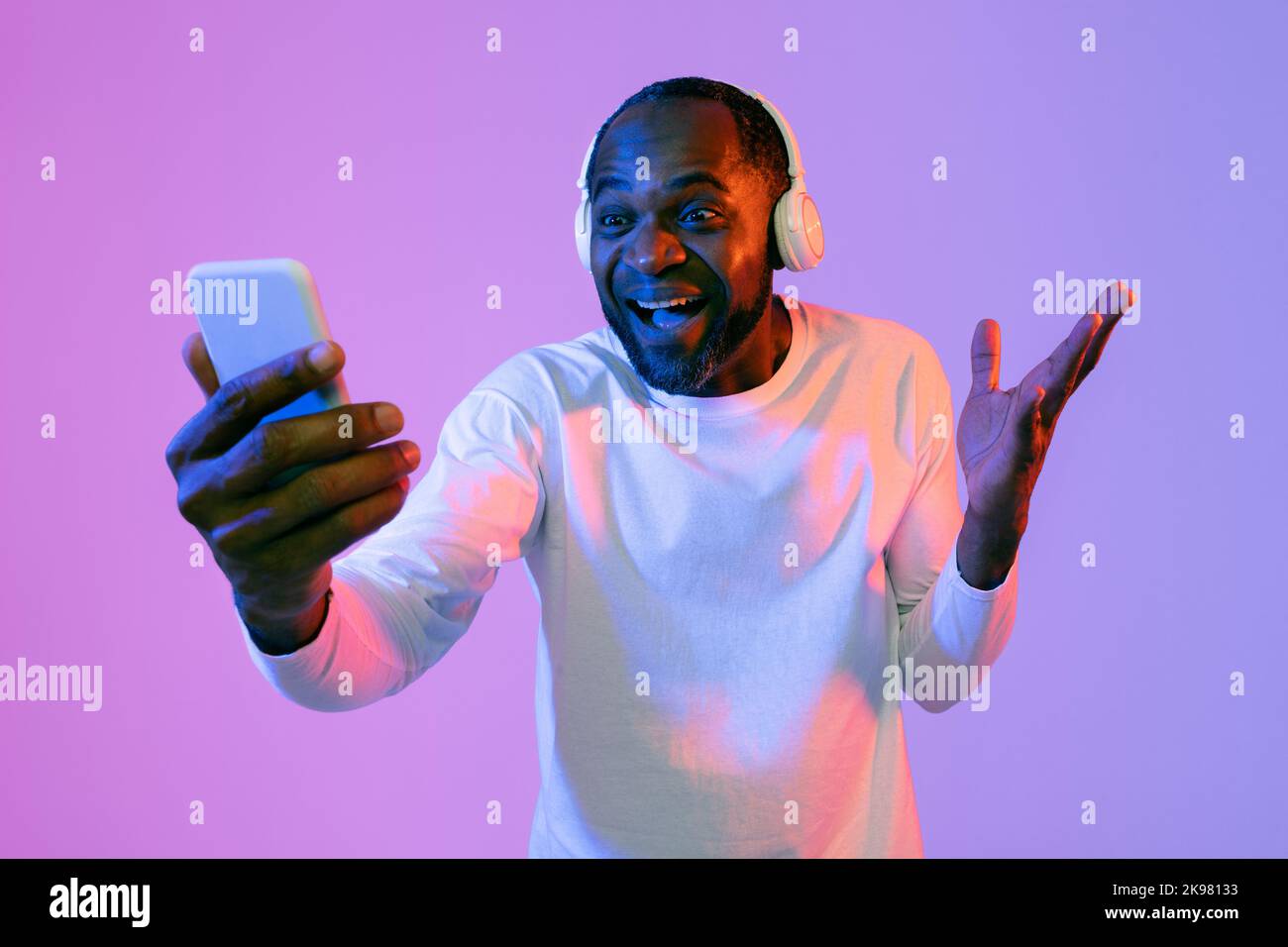 Emotional black man with wireless headset using smartphone Stock Photo