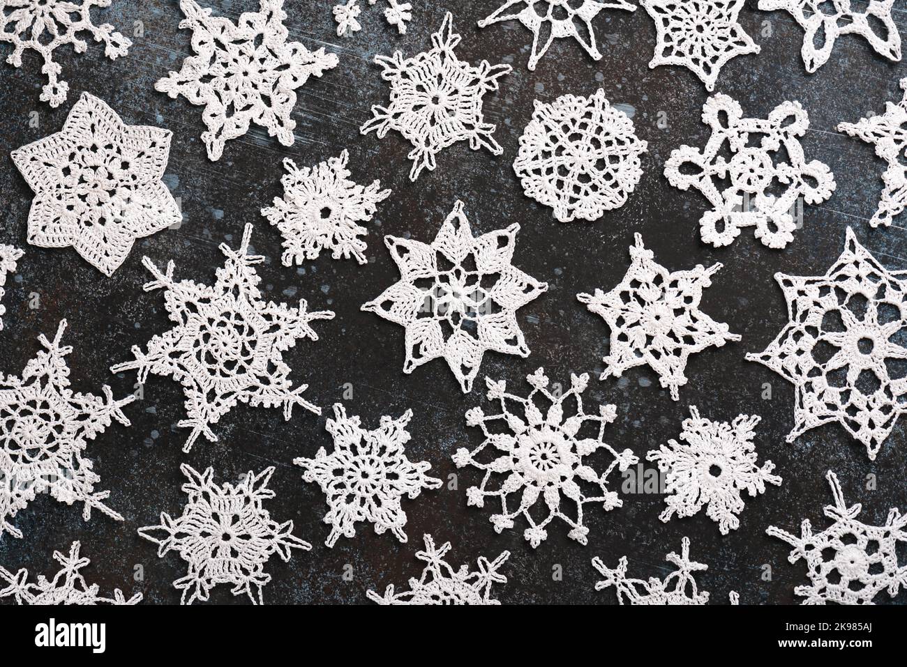 Beautiful varied white cotton crocheted stars and snowflakes on dark background. Easy handmade Christmas decoration or small gift. Flat lay. Stock Photo