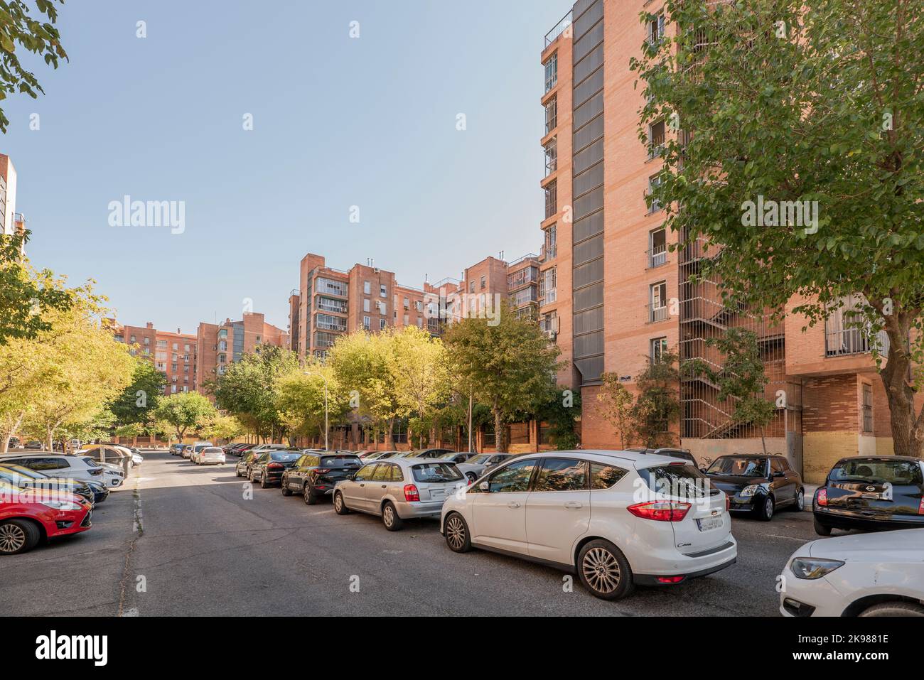 Facades of residential houses in urbanizations with many young trees and outdoor parking areas Stock Photo