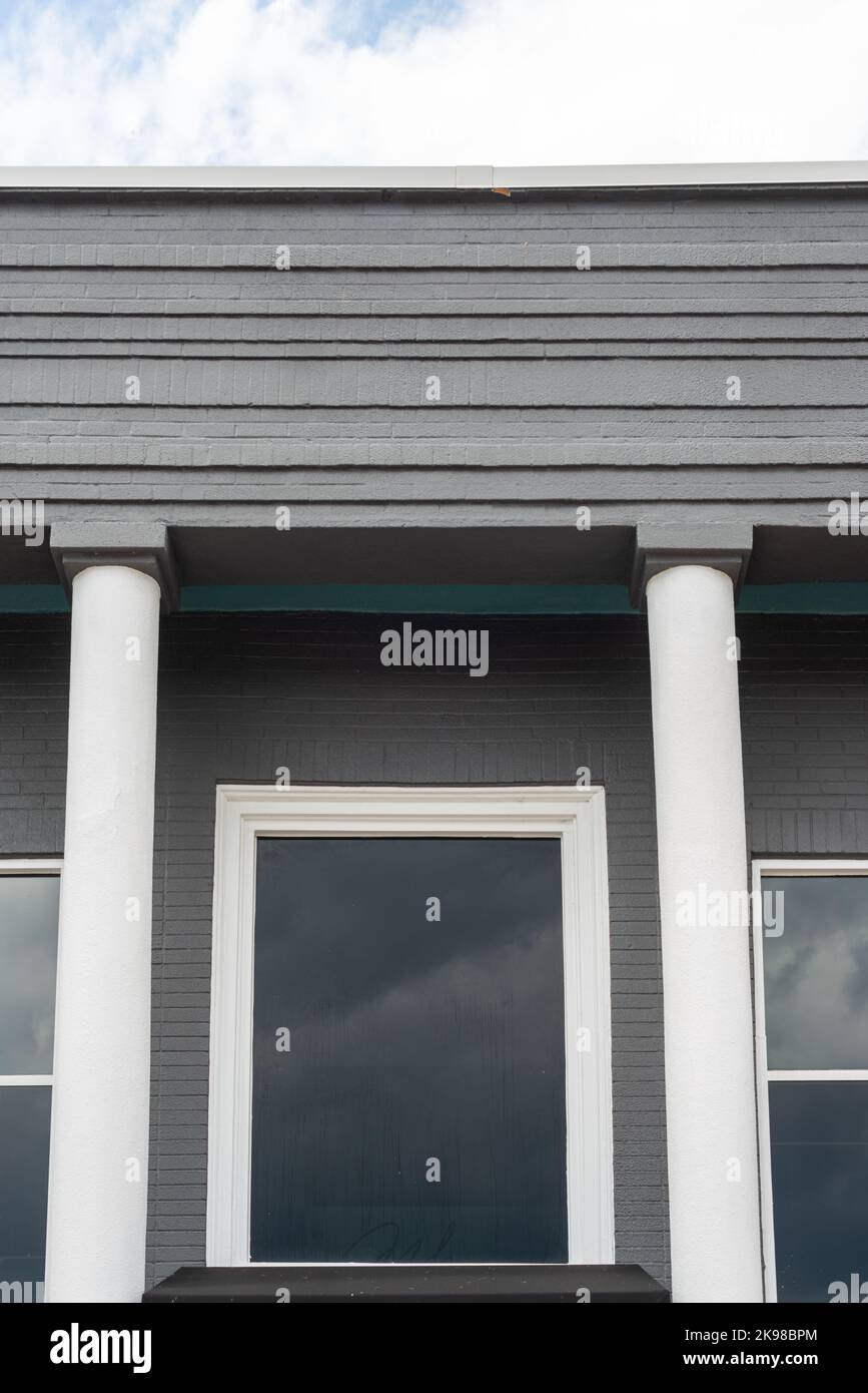 The roof section of an old grey colored cement business building wall. There are two white columns on either side of the door with two glass windows Stock Photo