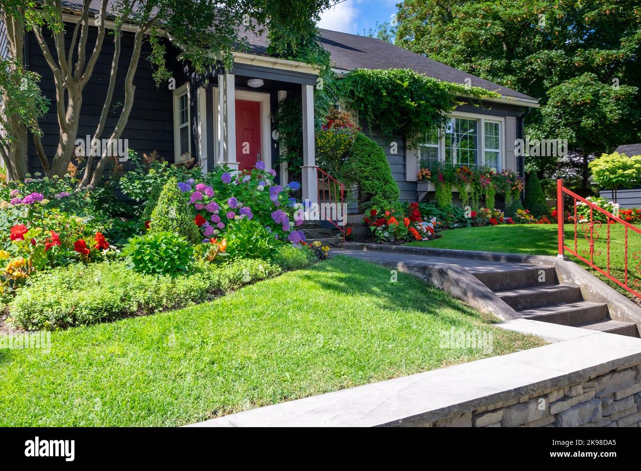 The front yard of a dark blue house with a vibrant red door. The