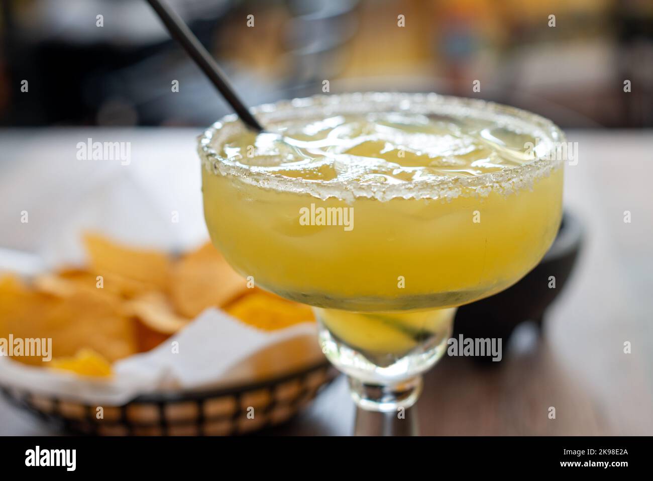 A closeup of a stepped-diameter margarita glass filled with a cold yellow alcohol liquid of tequila, ice, lemon juice, triple sec, and lime juice. The Stock Photo