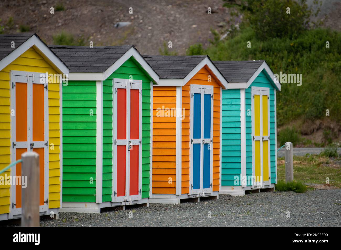 A row of small colorful painted huts or sheds made of wood. The exterior walls are colorful with double wooden doors. The sky is blue in the back Stock Photo