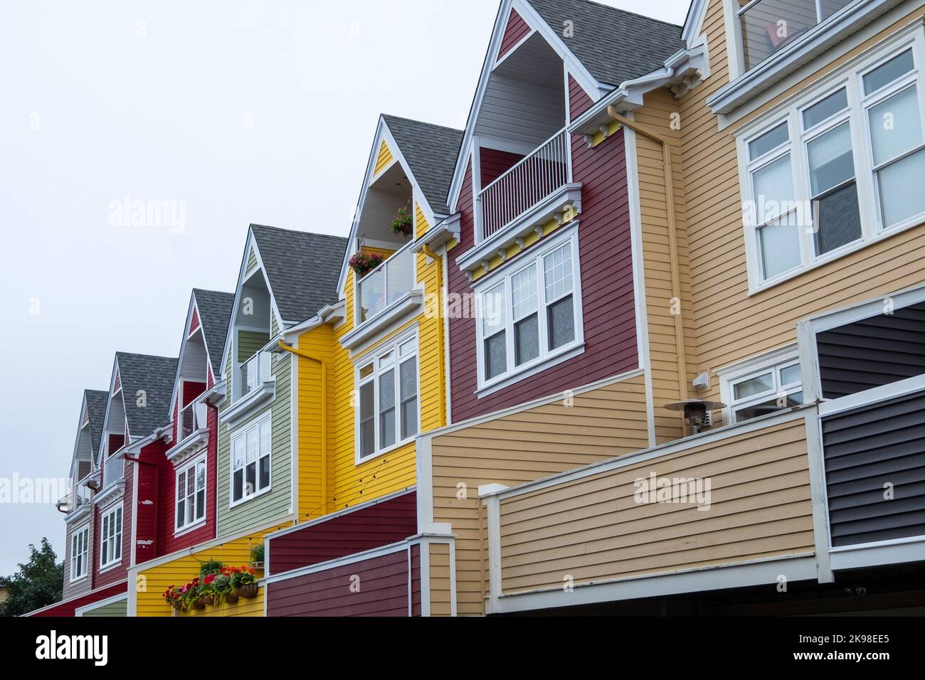 Street View of multiple colorful row houses in downtown St. John's. The buildings have peeked roofs, small windows, wood siding, and multiple layers. Stock Photo