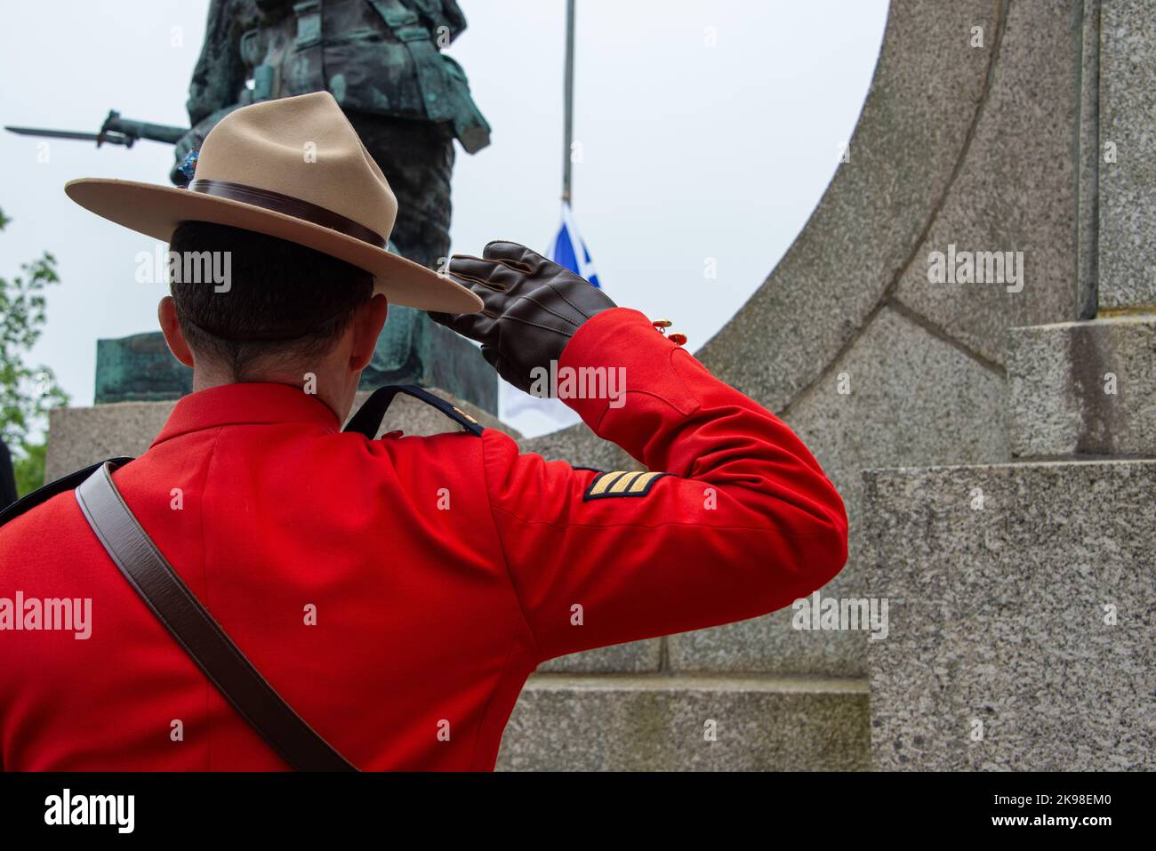 An RCMP officer stands at attention saluting during a ceremony. The serge uniform is vibrant red in color.The officer is wearing a tan colored Stetson Stock Photo
