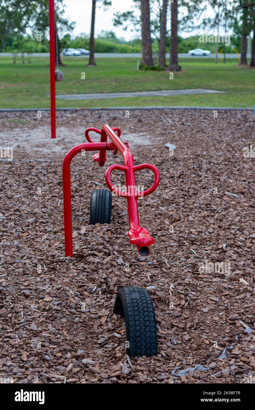 Colorful red metal durable children's playground equipment, teeter-totter, or seesaw in a park. The playground equipment moves up and down using a Stock Photo