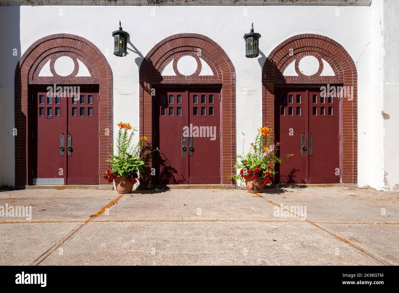 Three sets of red double doors with six small windows and a large door handle. The building is white stucco with vintage lanterns. Stock Photo