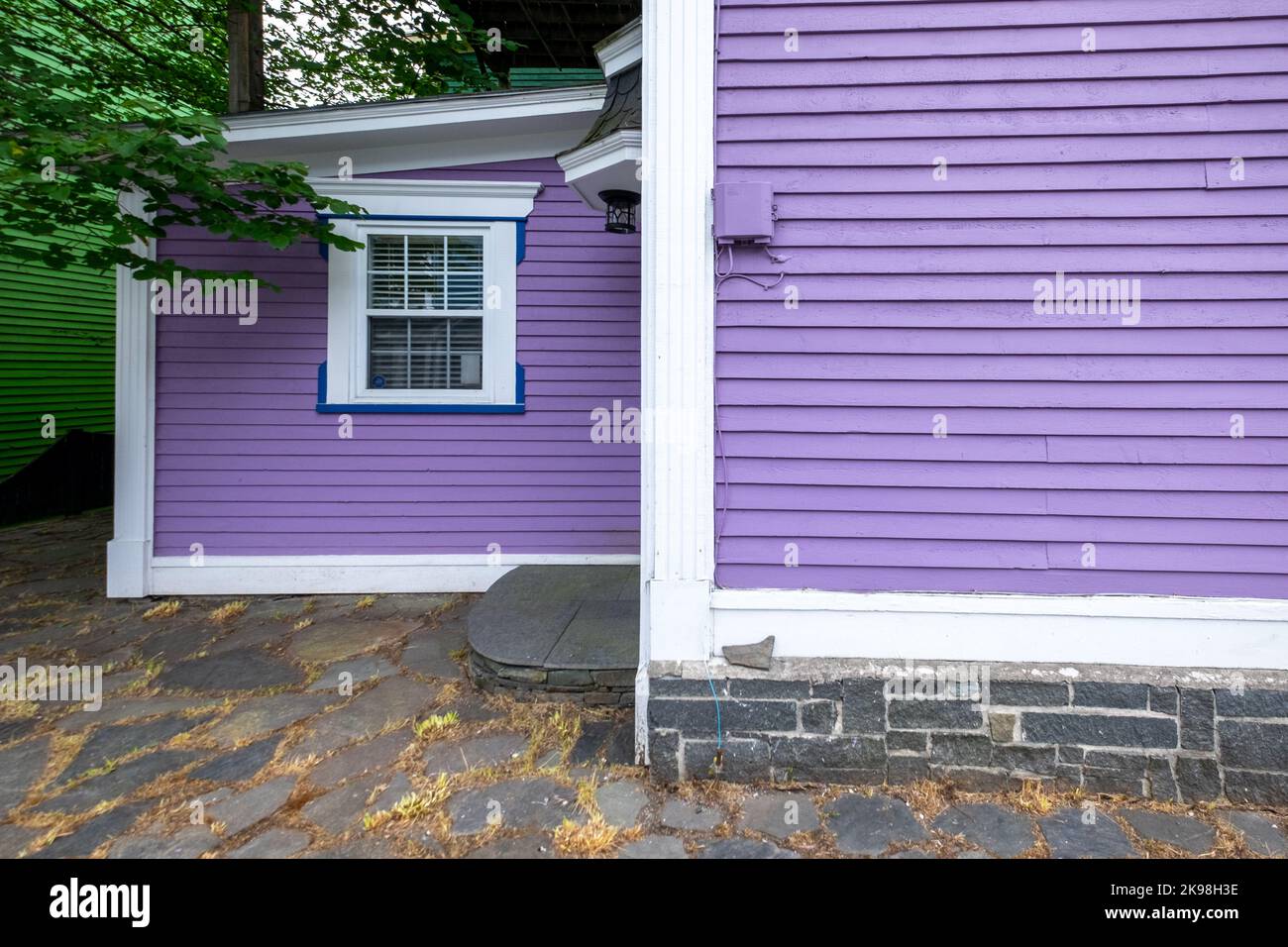 The exterior of a vibrant purple colored wooden wall covered in horizontal clapboard siding. The building has white trim with thin blue lines. Stock Photo