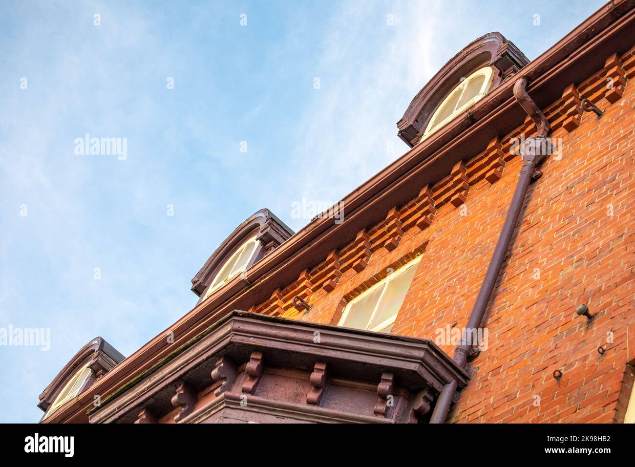 An upward view of a historic residential building with red brick, yellow and green wooden decorative style wood trim and glass single hung windows Stock Photo